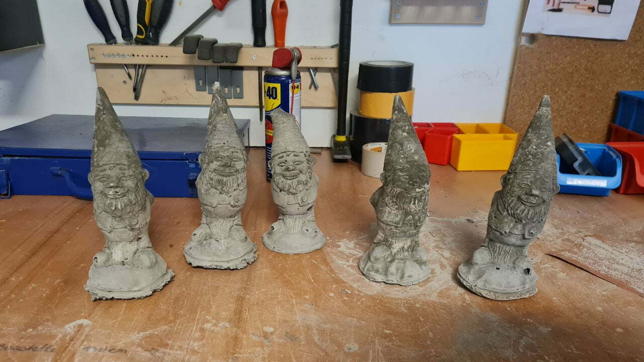 Fünf graue Gartenzwerge, die auf einem Werktisch stehen.